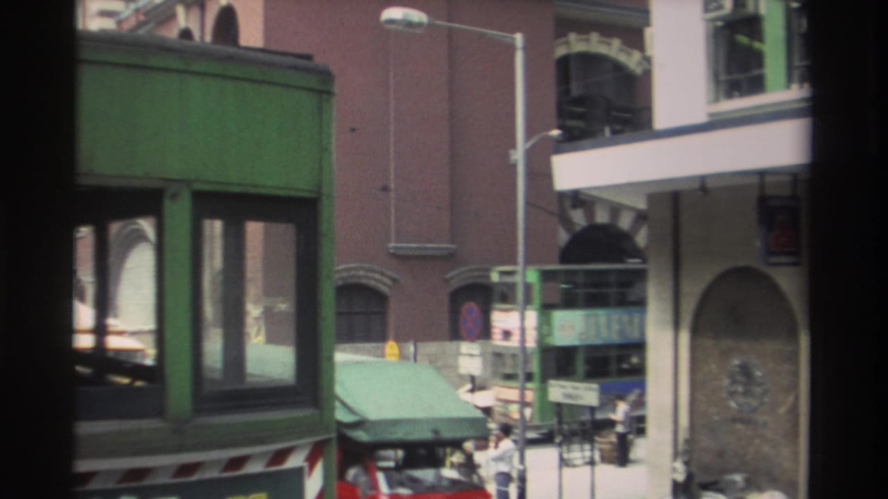 1982 Hong Kong street view with a green double-decker bus, pedestrians, arched building details, and storefront signage.