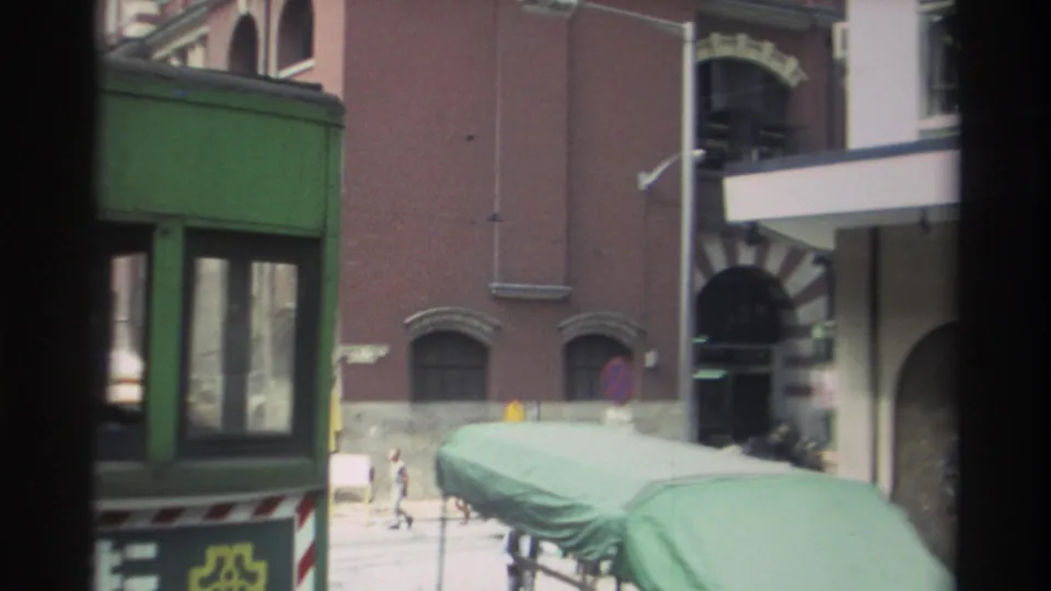 Hong Kong street scene from 1982 with green public transport vehicles, pedestrians, signs, and a large masonry building.