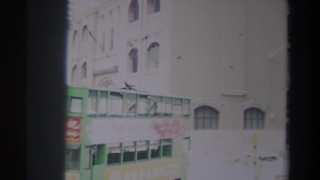 Green double-decker transit vehicle beside a building with arched windows and Chinese signage.