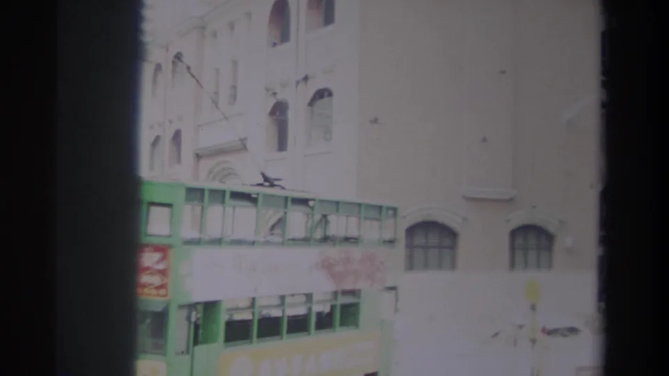 1982 Hong Kong street view with a green double-decker transit vehicle, overhead wires, shop signage and older building facades.
