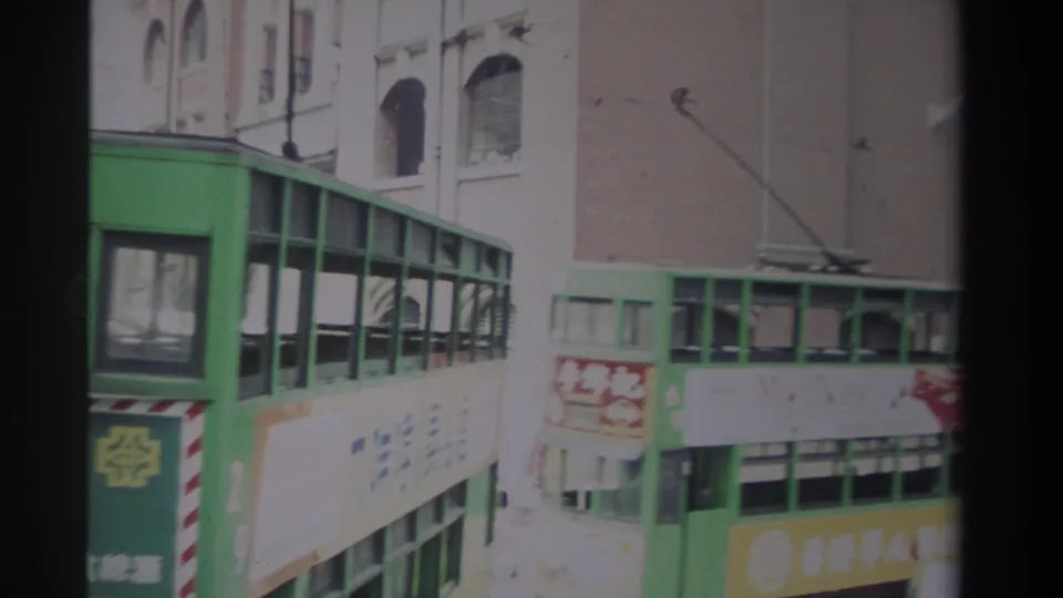 Close 1982 Hong Kong view of a green double-decker transit vehicle with side advertising, route signage and nearby street lamps.