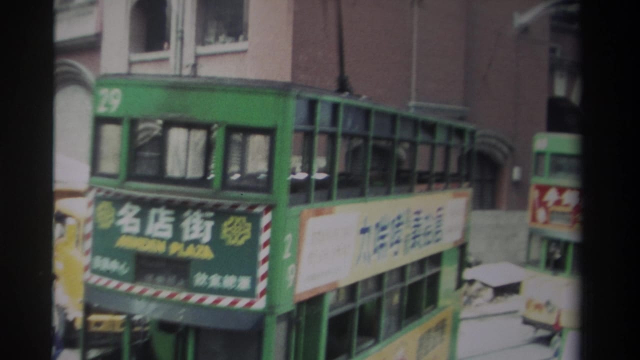 1982 Hong Kong street view with a green double-decker tram, Chinese signage, overhead trolley hardware, and brick building facades.
