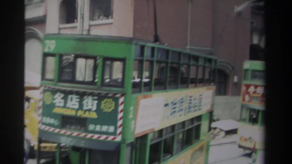 1982 Hong Kong street view with a green double-decker tram, Chinese signage, overhead trolley hardware, and brick building facades.