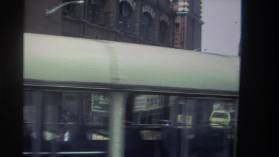 Close 1982 Hong Kong transit view with a bus passing in front of a covered walkway and vehicles beyond.