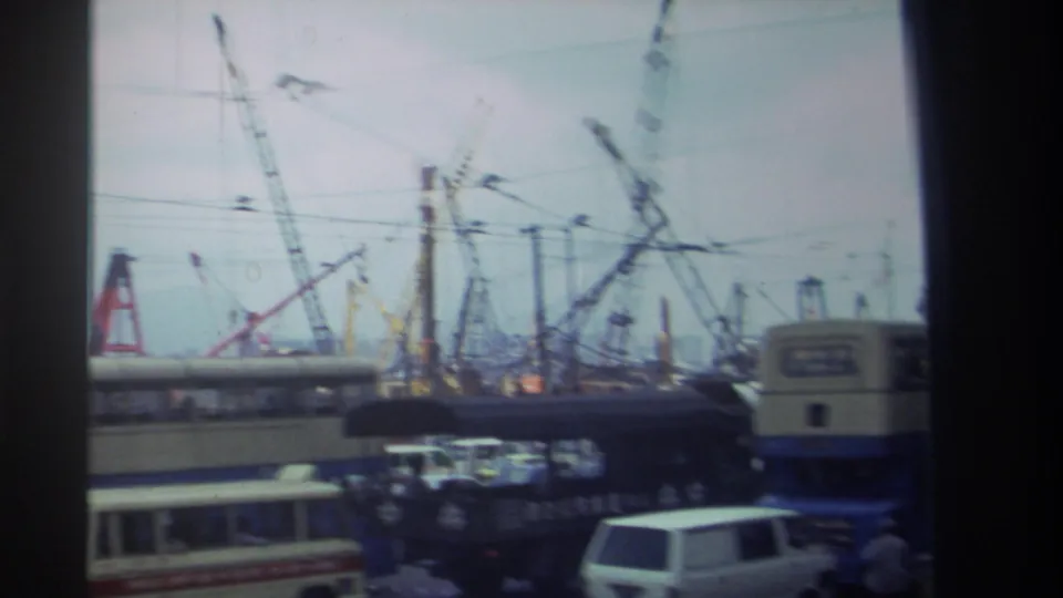 1982 Hong Kong traffic view with buses and vans below overhead wires and multiple construction cranes.
