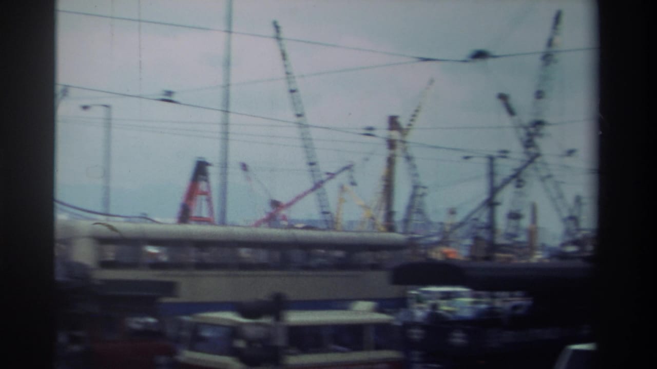 Hong Kong street view from 1982 with cranes, overhead wires, cars, and a motion-blurred bus passing in the foreground.