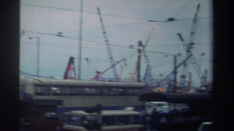 Hong Kong street view from 1982 with cranes, overhead wires, cars, and a motion-blurred bus passing in the foreground.
