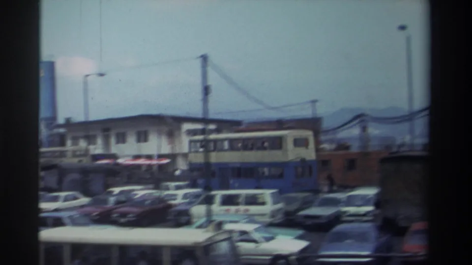 Hong Kong street view from 1982 with a double-decker bus, parked cars, overhead wires, cranes, and low buildings.