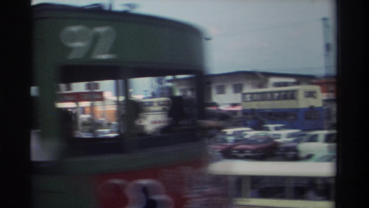 Double-decker bus passing close to the camera with cars and street buildings behind it.