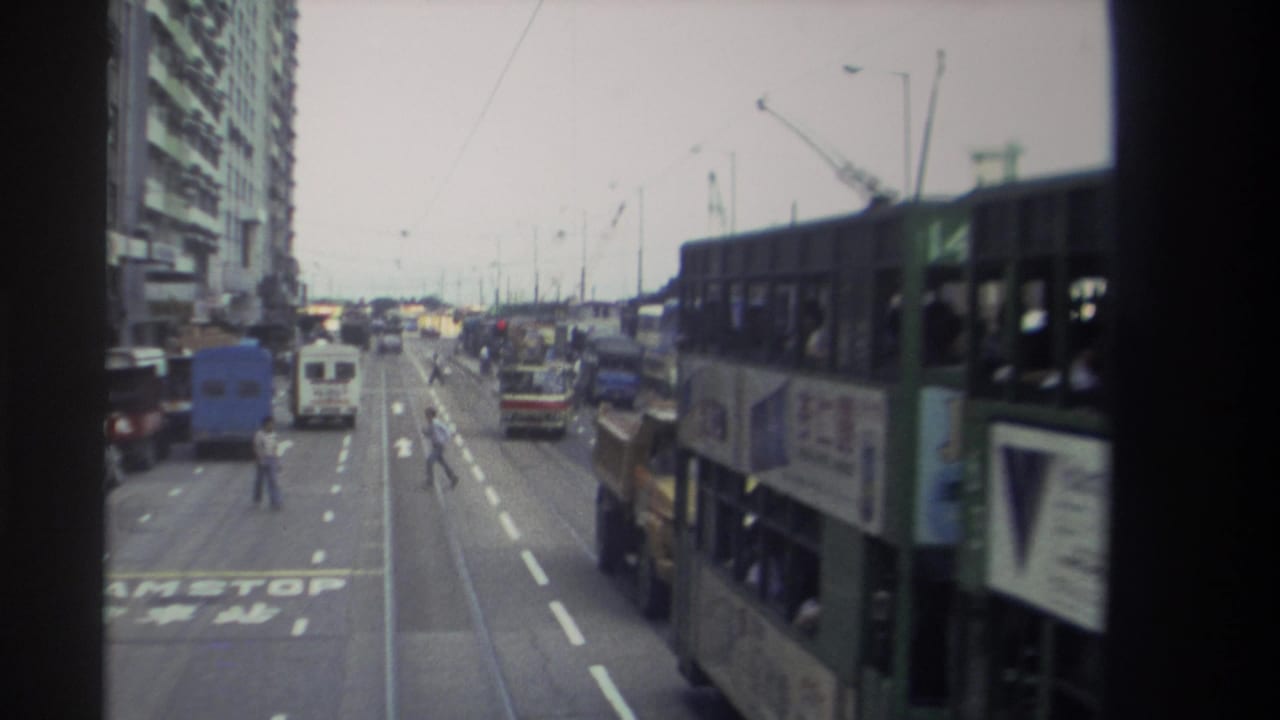 1982 Hong Kong street view from a moving vehicle, showing tram tracks, double-decker buses, trucks, vans, road markings, and a pedestrian.