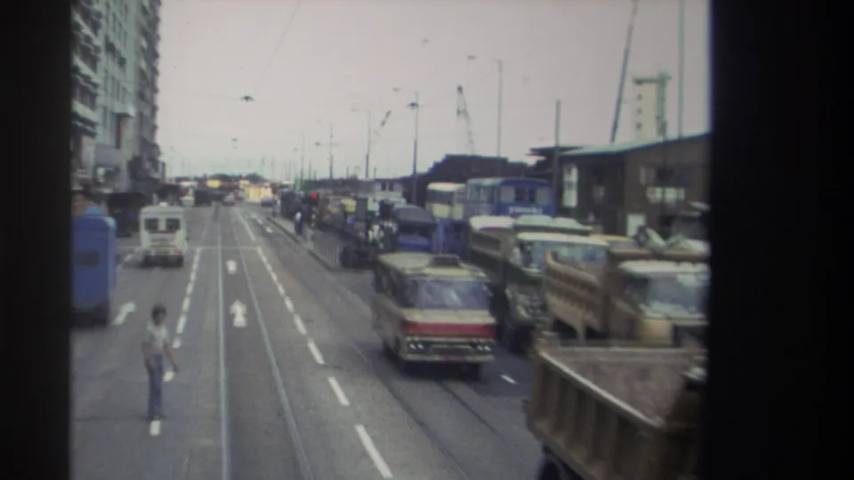 1982 Hong Kong road scene with a pedestrian crossing, tram tracks, buses, trucks, vans, traffic lanes, and overhead street wires.