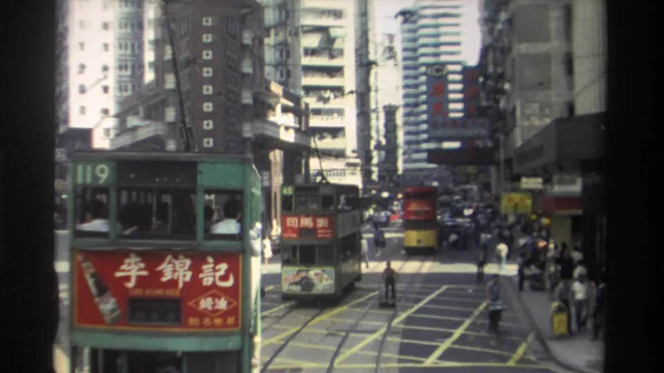 Close 1982 Hong Kong view of a green route 119 double-decker tram with a red advertisement, with traffic, pedestrians, and buildings beyond.