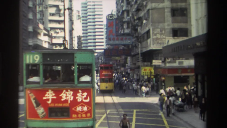 1982 Hong Kong street frame with green tram 119, red Lee Kum Kee signage, pedestrians, shopfronts, and high-rise buildings.