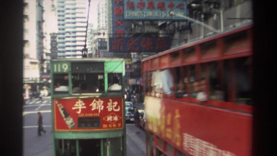 1982 Hong Kong street traffic with a green double-decker tram, red bus, Chinese signage, and pedestrians along the sidewalk.