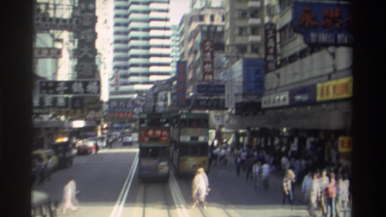 1982 Hong Kong street view with a double-decker tram traveling along tracks, pedestrians near the curb, older cars, and dense Chinese signage on surrounding buildings.