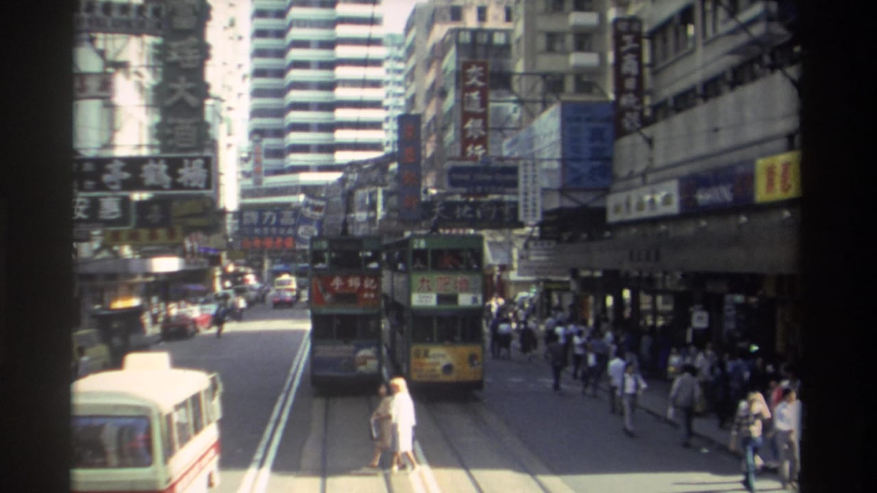 1982 Hong Kong traffic scene showing a tram moving down the tracks, a cream minibus in the foreground, pedestrians along the sidewalk, and layered Chinese commercial signs.