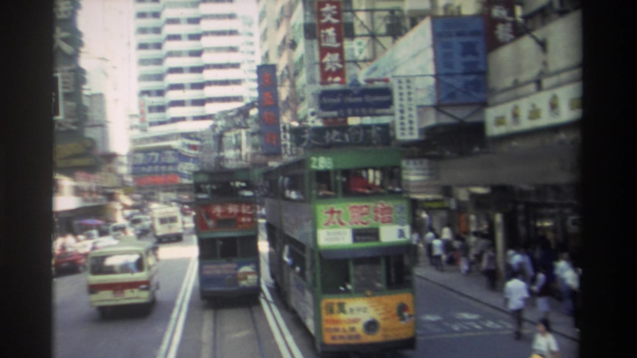 Busy Hong Kong street with cars, pedestrians, signs, and a green double-decker tram ahead.