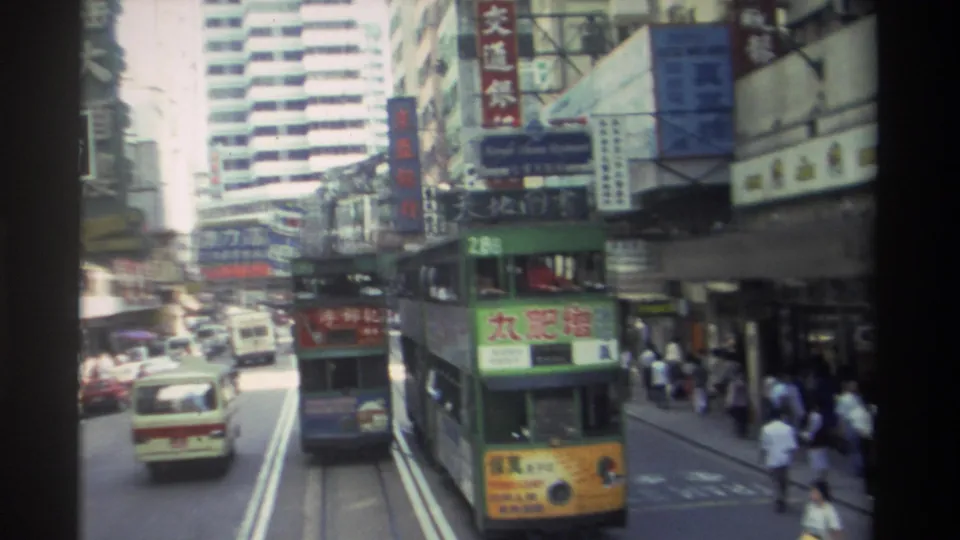 1982 Hong Kong street view with a green double-decker tram, cars, pedestrians, and dense vertical Chinese signage along narrow buildings.