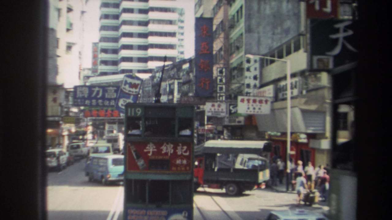 Double-decker tram and busy street traffic seen between buildings and shop signs.