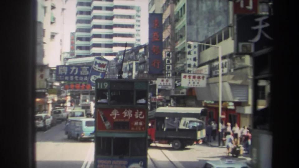 Hong Kong street traffic in 1982, with a double-decker tram, vans, cars, pedestrians, and layered Chinese-character signage.
