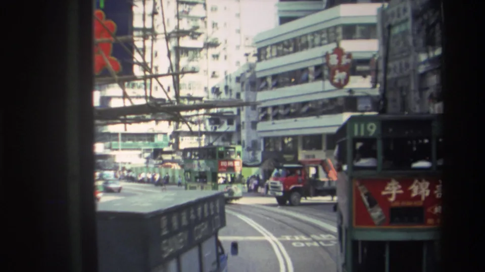 Busy 1982 Hong Kong roadway with tram tracks, commercial signs, vans, pedestrians, and part of a route 119 tram at the edge.