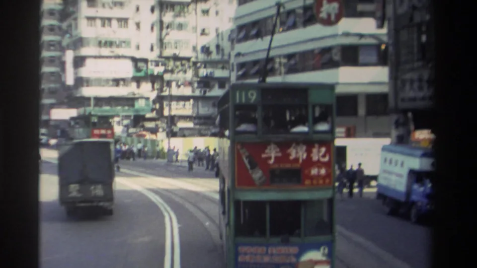 1982 Hong Kong traffic scene with a route 119 double-decker tram, dark truck, blue vehicle, pedestrians, and commercial signage.
