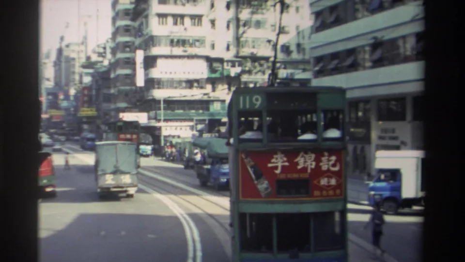 1982 Hong Kong frame with a route 119 double-decker tram, road traffic, pedestrians, tram tracks, and dense commercial buildings.