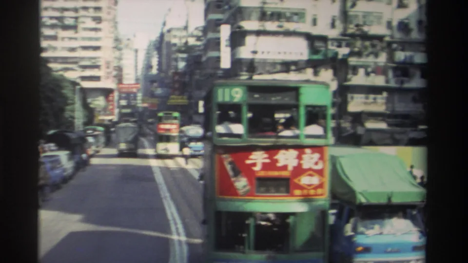 Two route-119 Hong Kong double-decker trams running alongside on tram tracks through a dense urban streetscape, red Lee Kum Kee advertisement panels visible, 1982 8mm footage.