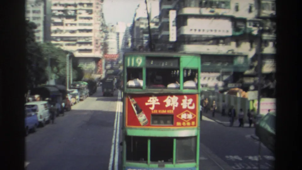 Hong Kong tram route 119 moving along a busy urban street, circa 1982, with Lee Kum Kee advertisement, parked vehicles, and densely packed tower blocks behind.