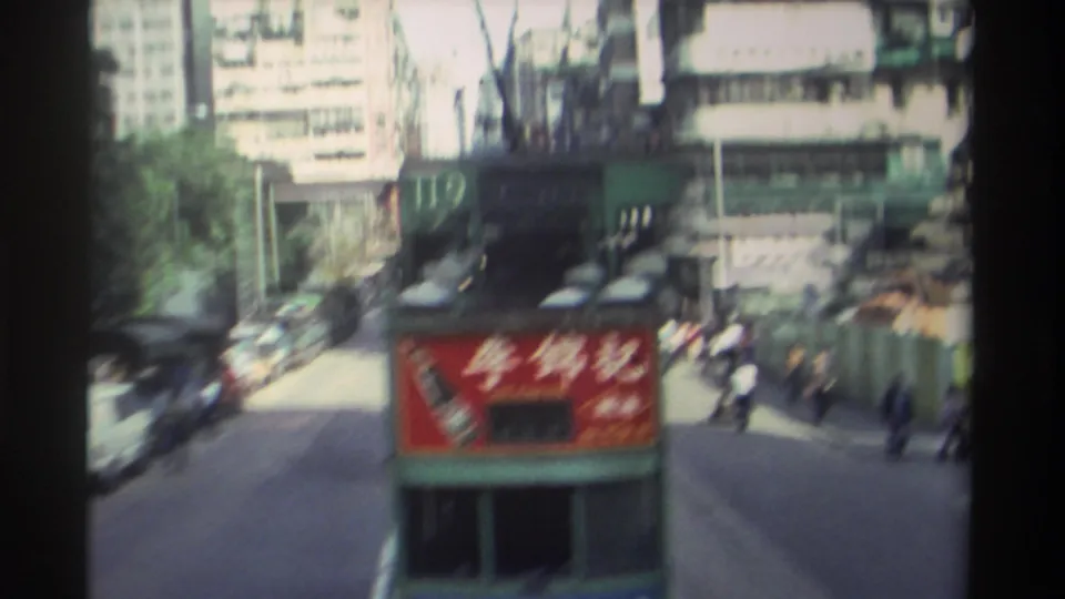 Motion-blurred frame of Hong Kong tram route 119 departing along a commercial street, circa 1982, with pedestrians, Lee Kum Kee panel, and urban buildings visible.