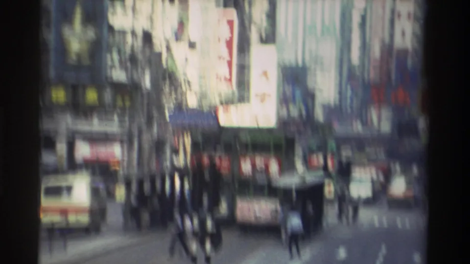 Handheld camera pan creates heavy motion blur across a Hong Kong street, 1982 — Chinese signs and moving figures smeared across the frame.