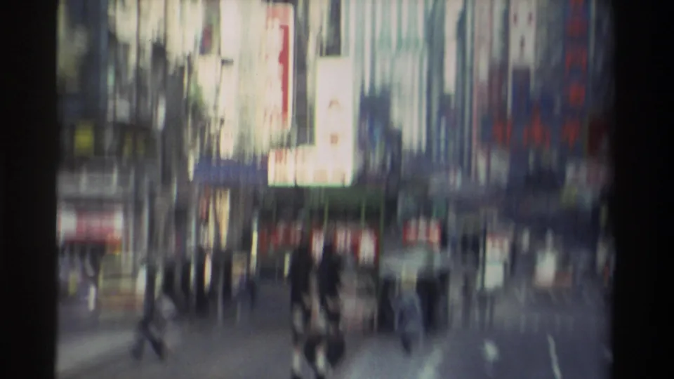 Final frame of 1982 Hong Kong 8mm clip — sustained camera pan blurs pedestrians and street-level Chinese signage into layered motion streaks.