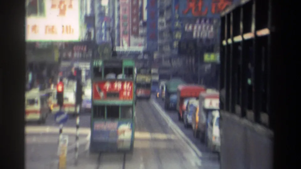 Elevated 1982 Hong Kong street view with green double-decker trams and vintage vehicles amid densely signposted commercial buildings.