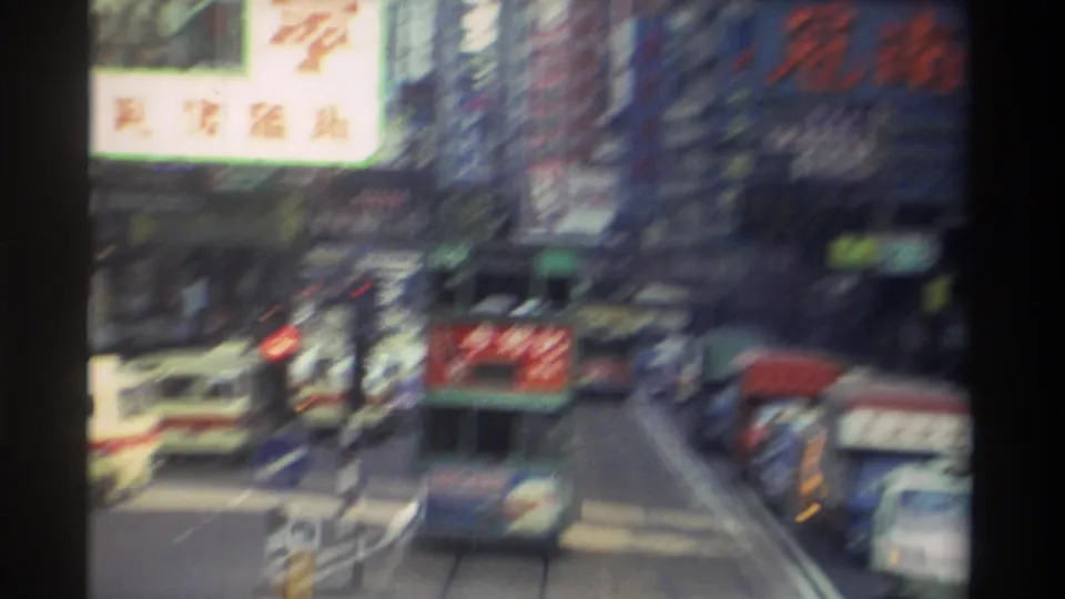 Motion-blurred frame from a 1982 Hong Kong street pan showing green trams and illuminated Chinese commercial signage.