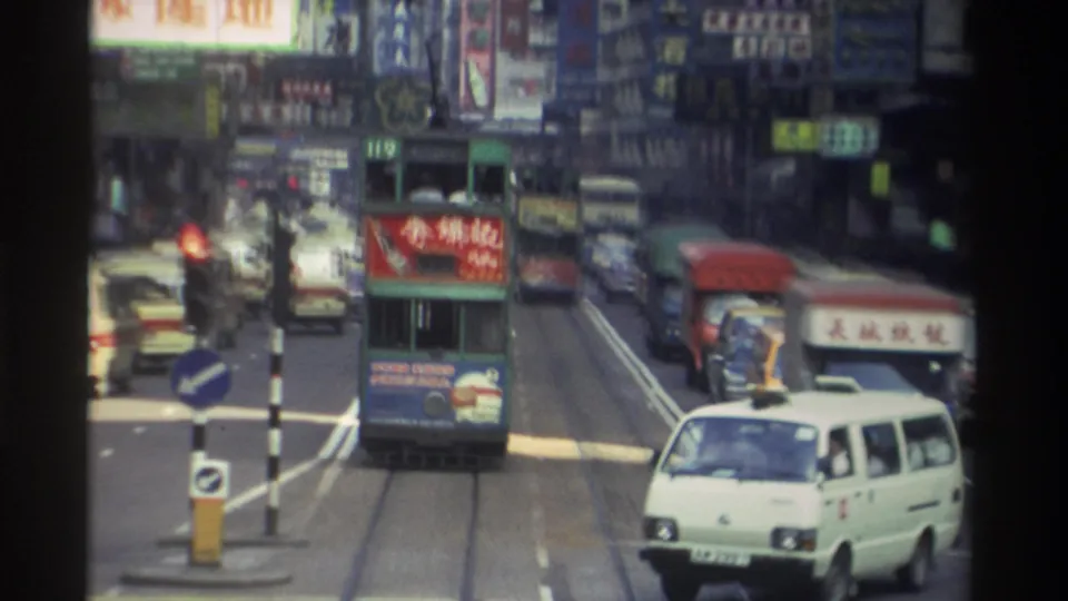 1982 Hong Kong street scene with tram No. 119, a white vintage van, heavy goods vehicles, and wall-to-wall Chinese commercial signage on building facades.