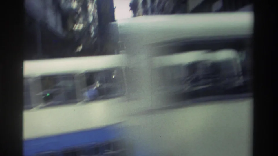 White and blue double-decker vehicle — likely the tram seen in earlier frames — filling the frame as it passes the camera in 1982 Hong Kong, with strong motion blur.