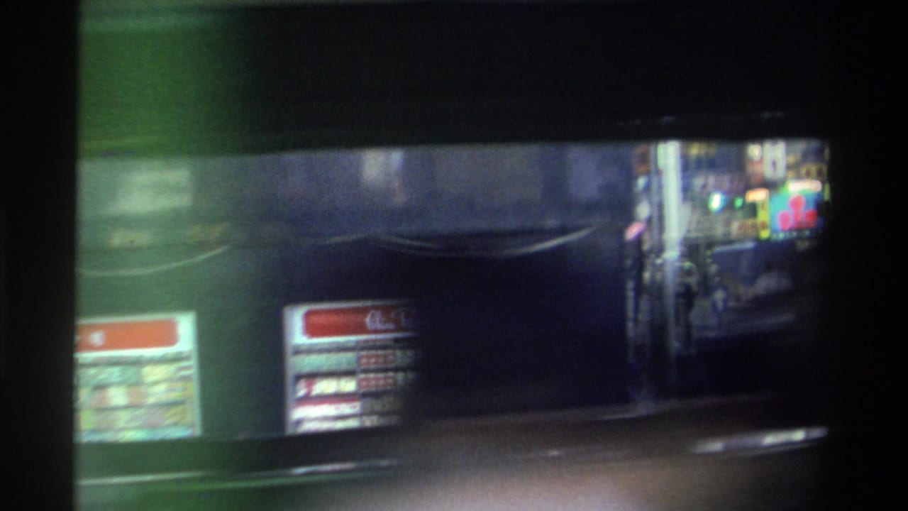 Close view of a green double-decker bus or tram body filling the frame, with a red destination board bearing Chinese characters; neon signs visible in background.
