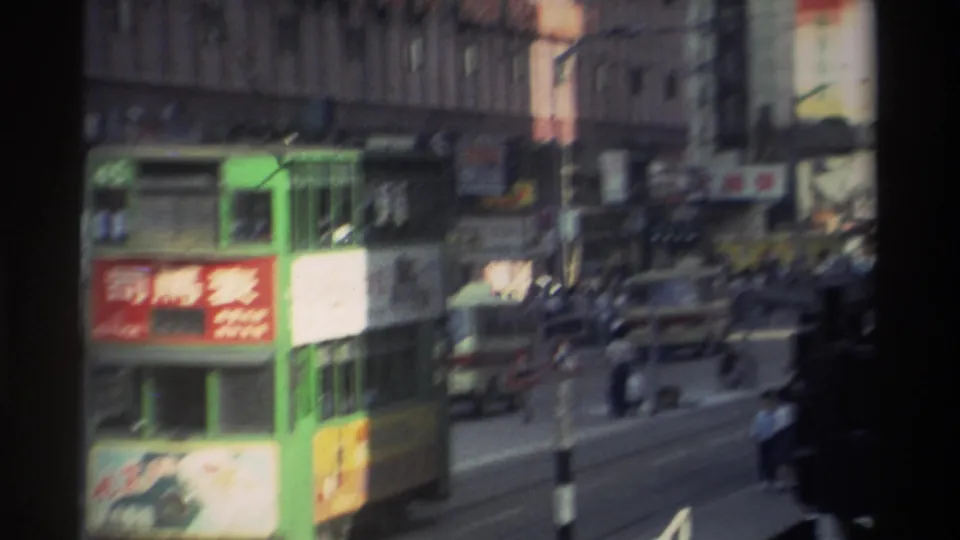 Looking along a Hong Kong street in 1982: green trams, dense Chinese shopfront signage, a Coca-Cola advertisement and overhead tram wires visible from a moving vehicle.