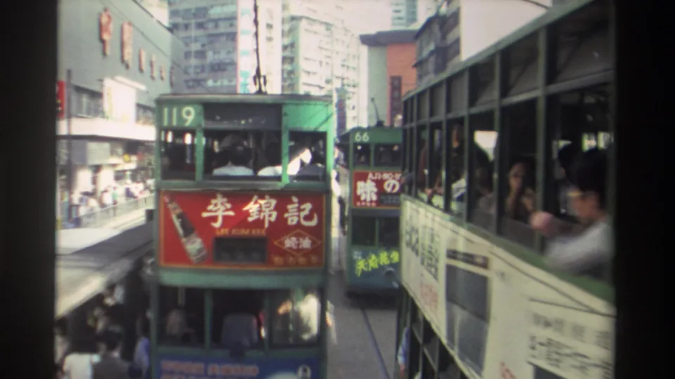 Close view of trams 119 and 66 on a Hong Kong street in 1982, red Lee Kum Kee soy sauce panel filling the tram side, pedestrians in motion blur, commercial buildings visible behind.