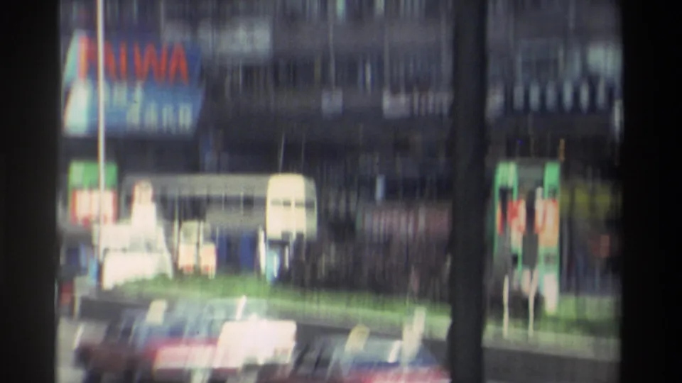 Motion-blurred view of dense Hong Kong traffic showing an AIWA billboard and double-decker bus filmed from a moving tram, circa 1982.