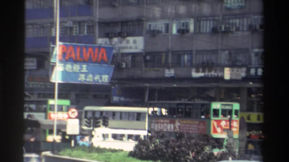 Elevated view of a Hong Kong street circa 1982 showing a PALWA billboard, multiple green trams, Chinese-character signage, and a white minibus in dense traffic.