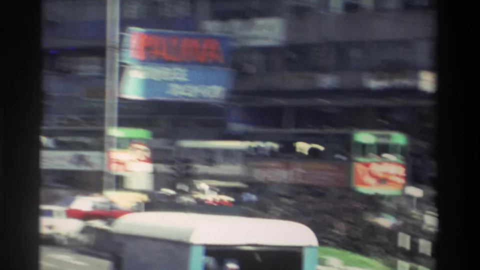 Motion-blurred Hong Kong tram-street scene with green trams, red and colourful advertising billboards, and dense Chinese-character urban signage, circa 1982.