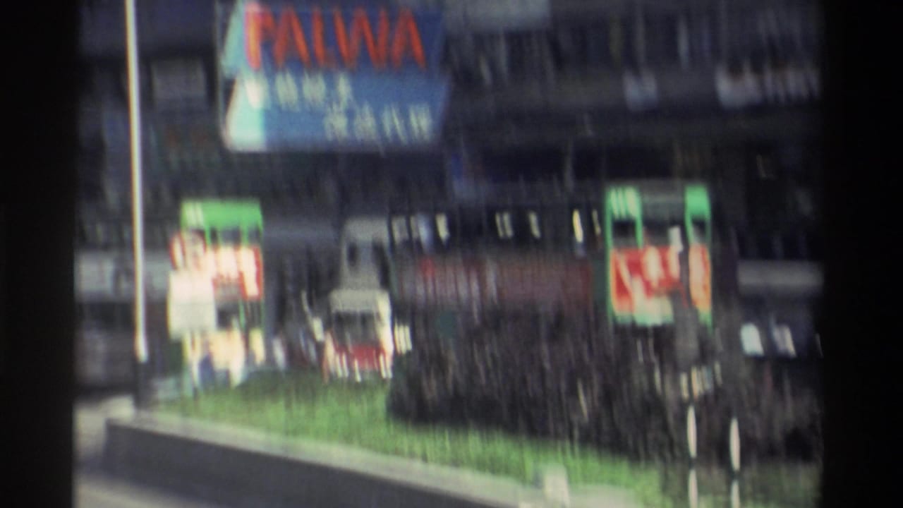 PALWA sign and dense commercial billboards on a Hong Kong street, with a green median strip and tram roof visible below.