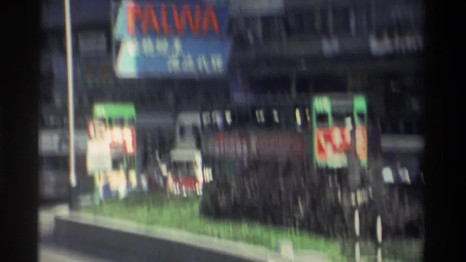 8mm frame from Hong Kong, 1982, showing the PALWA sign prominently above multiple commercial billboards; a green street median and tram roof are visible at lower frame.