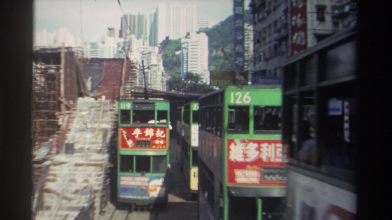 Green double-decker trams pass through a narrow street beside construction scaffolding.
