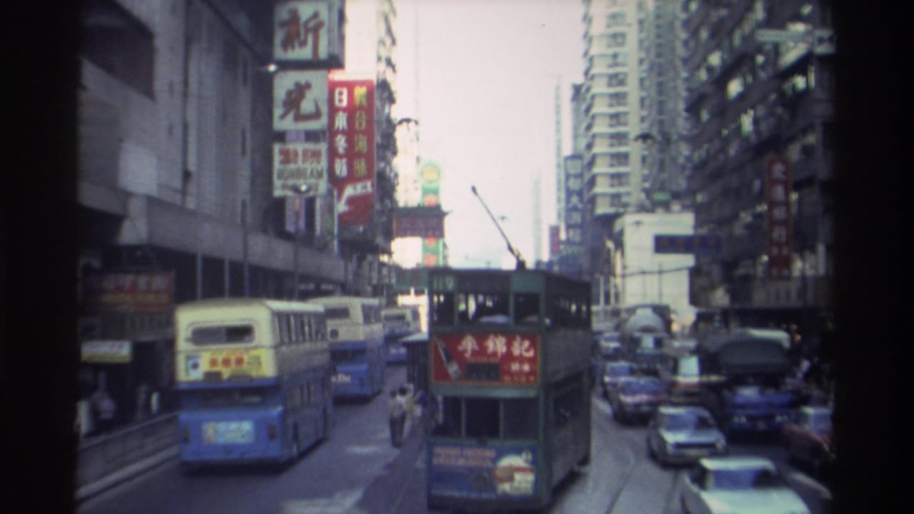Hong Kong street with double-decker buses navigating traffic beneath tall buildings and Chinese signs, 1982.