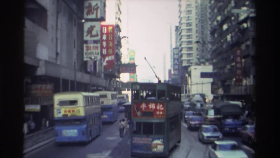 1982 Hong Kong: double-decker buses navigate busy traffic as tall residential and commercial buildings display dense layered Chinese signage.