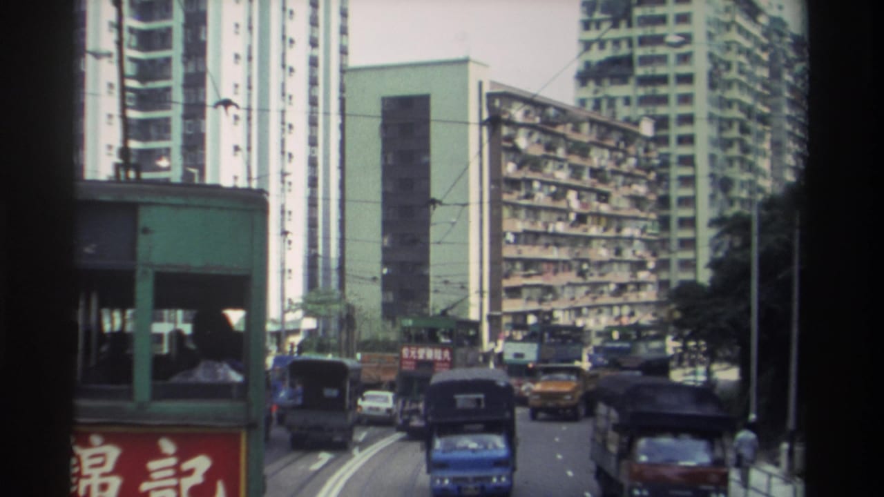 Hong Kong tram corridor with tram ahead, red Chinese 錦記 signage, apartment towers, and street traffic filmed from a moving tram, 1982.