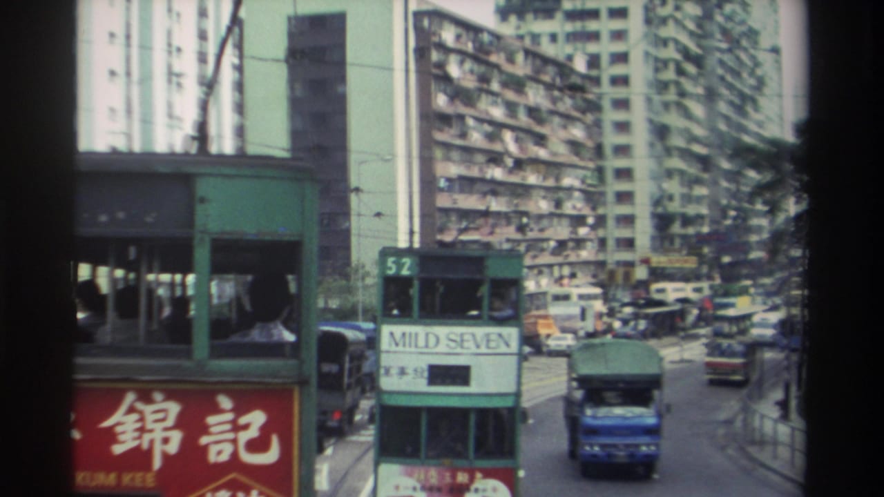 Route 52 green double-decker tram bearing a 'MILD SEVEN' advertisement, shot from a moving vehicle on a crowded Hong Kong street circa 1982, with laundry-draped tower blocks behind.