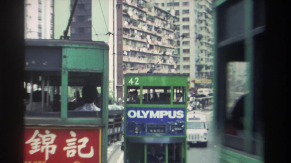 Route 42 Hong Kong double-decker tram bearing an 'OLYMPUS' camera brand advertisement; dense residential high-rises with hanging laundry fill the background, circa 1982.